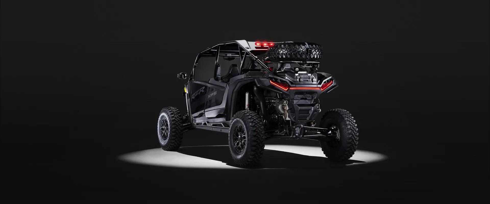 Rear view of an Onyx Black 2027 Polaris RZR XP S 4 side-by-side entrenched in light in a dark room.