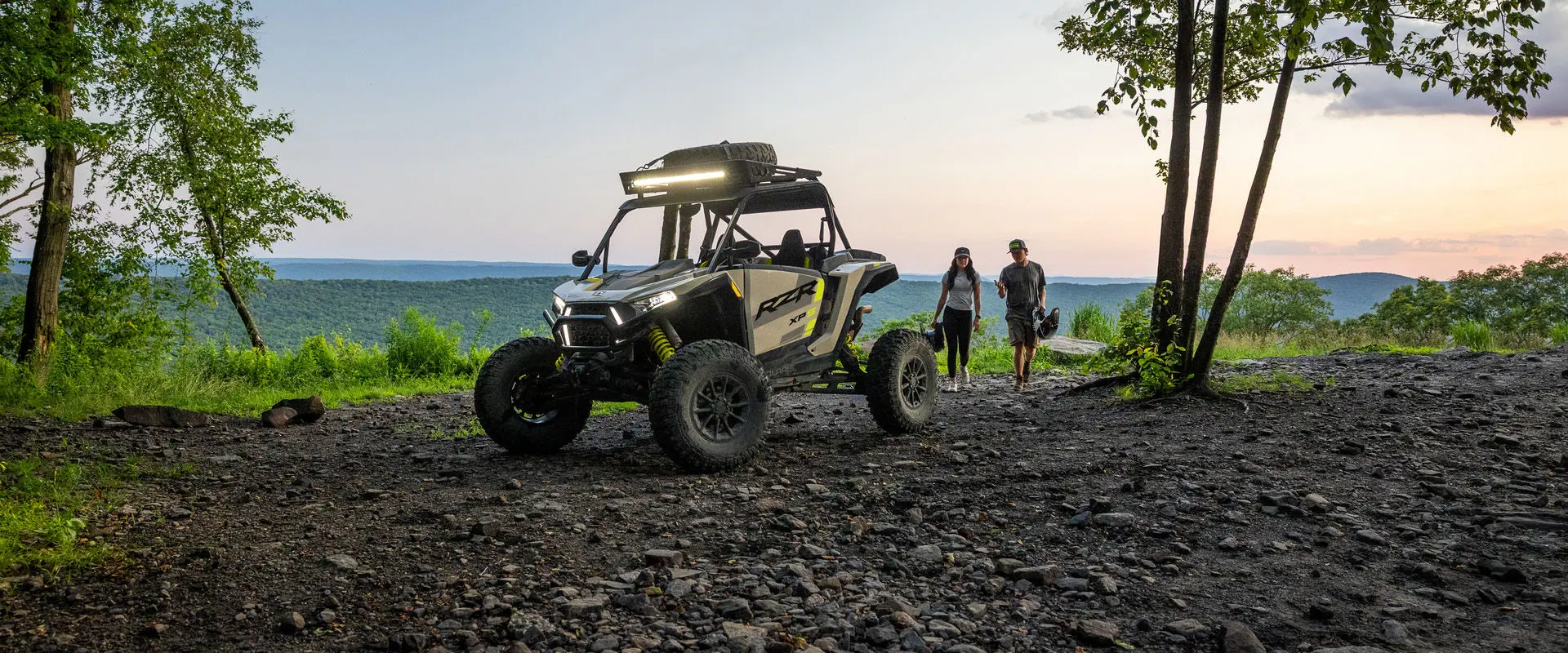 2 people walking toward a 2027 Polaris RZR XP S side-by-side with accessories and light bar installed.