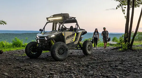 2 people walking toward a 2027 Polaris RZR XP S side-by-side with accessories and light bar installed.