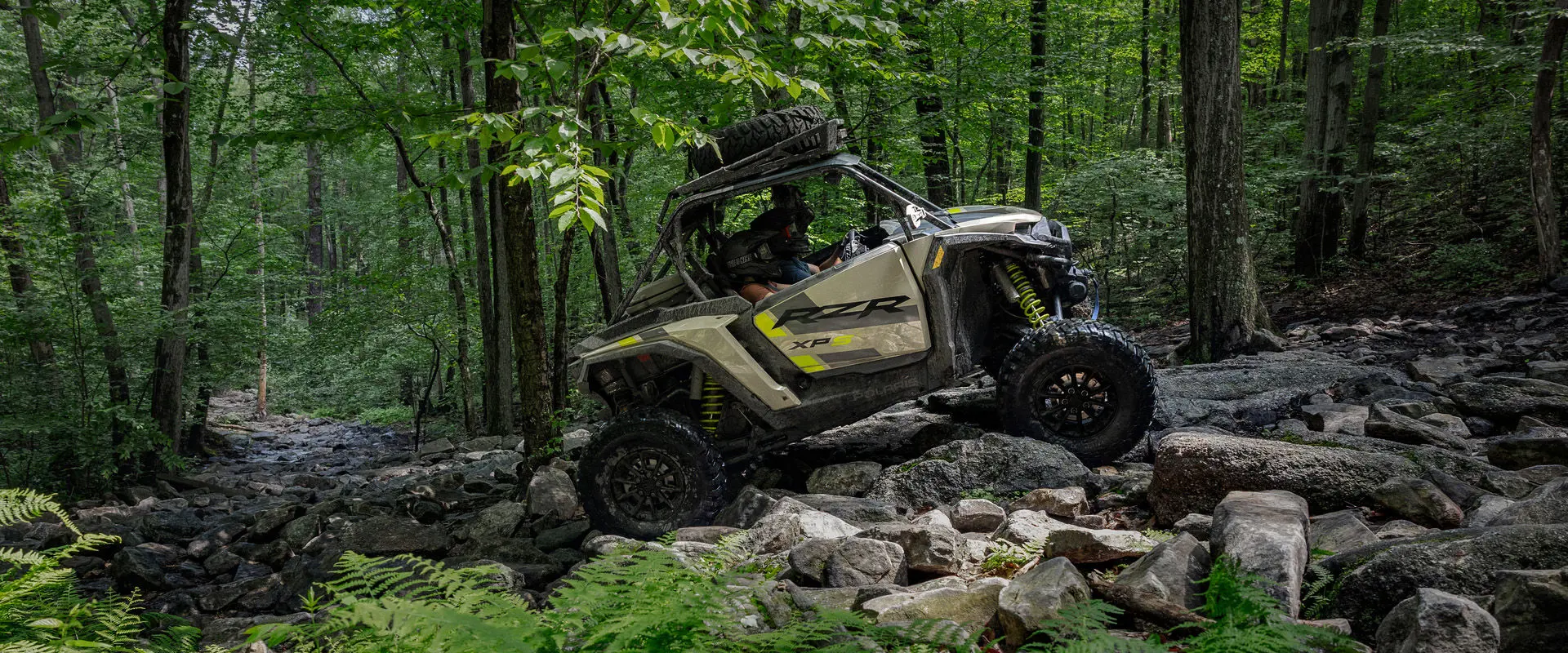 Side profile of a 2027 Polaris RZR XP S Ultimate side-by-side crawling over rocky terrain.