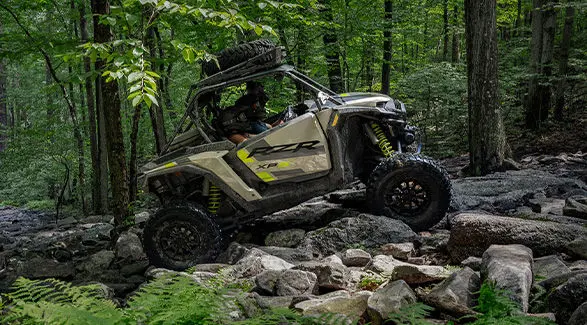 Side profile of a 2027 Polaris RZR XP S Ultimate side-by-side crawling over rocky terrain.