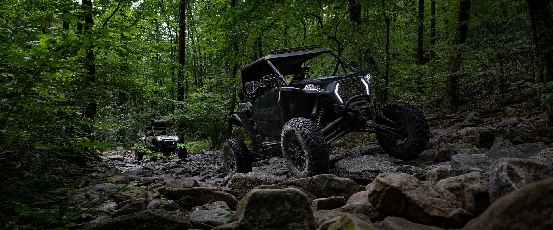 2 riders in a 2027 Polaris RZR XP S side-by-side crawling over rocky terrain.