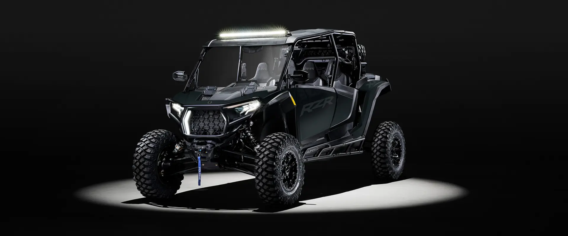 A 2027 Polaris RZR XP 4 Ultimate side-by-side with a light bar accessory entrenched in light while parked in a dark garage.