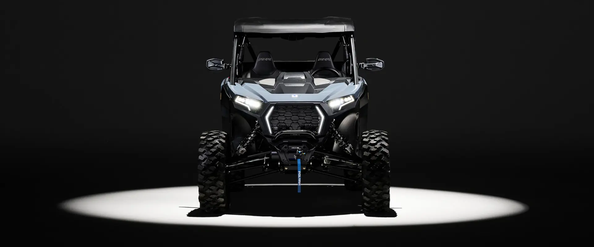 Front end view of a 2027 Polaris RZR XP Ultimate SxS entrenched in light while parked in a dark garage.