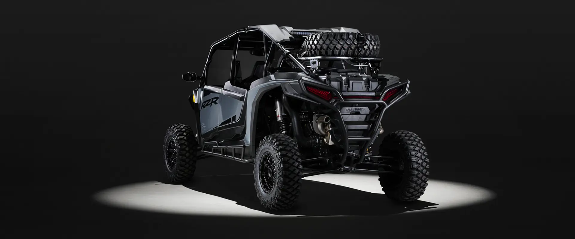 Rear view of a 2027 Polaris RZR XP 4 Ultimate SxS entrenched in light while parked in a dark garage.
