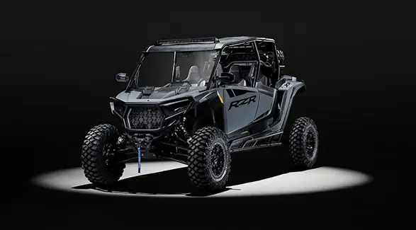 Angled view of a 2027 Polaris RZR XP 4 Ultimate SxS entrenched in light and parked in a dark garage.
