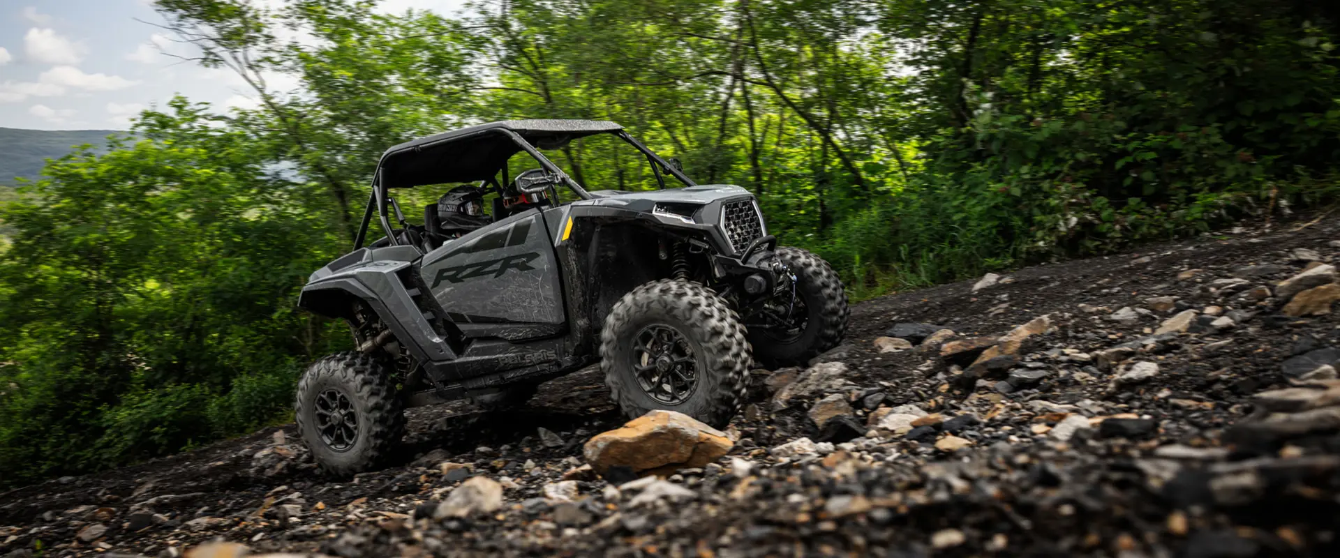 A 2027 Polaris RZR XP Ultimate SxS climbing over rough rocky terrain.