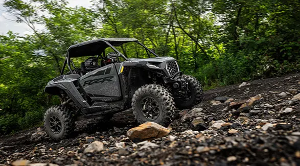 A 2027 Polaris RZR XP Ultimate SxS climbing over rough rocky terrain.