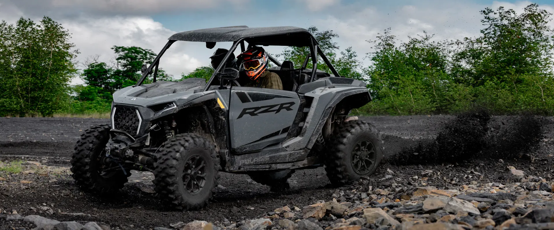 2 riders in a 2027 Polaris RZR XP Ultimate SxS throwing mud on a sunny day.