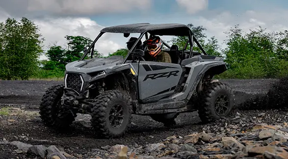 2 riders in a 2027 Polaris RZR XP Ultimate SxS throwing mud on a sunny day.