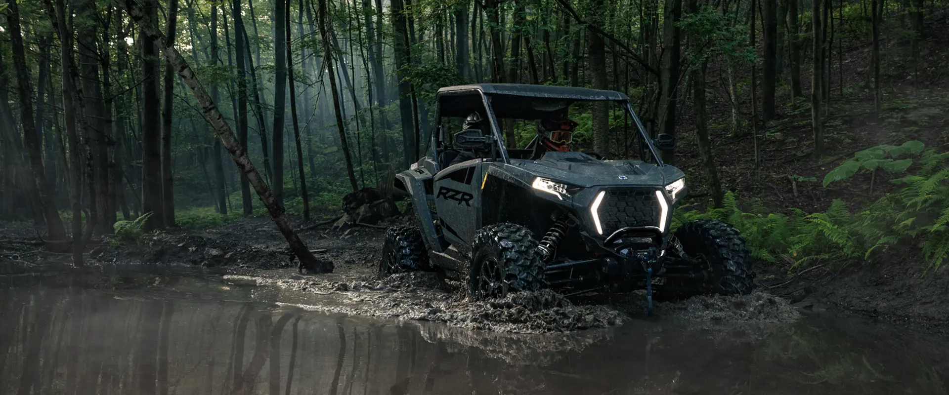 A 2027 Polaris RZR XP Ultimate SxS with illuminated lights crawling through a mudhole.