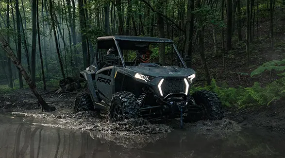 A 2027 Polaris RZR XP Ultimate SxS with illuminated lights crawling through a mudhole.