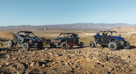 Three Polaris RZR Pro vehicles on a rocky landscape