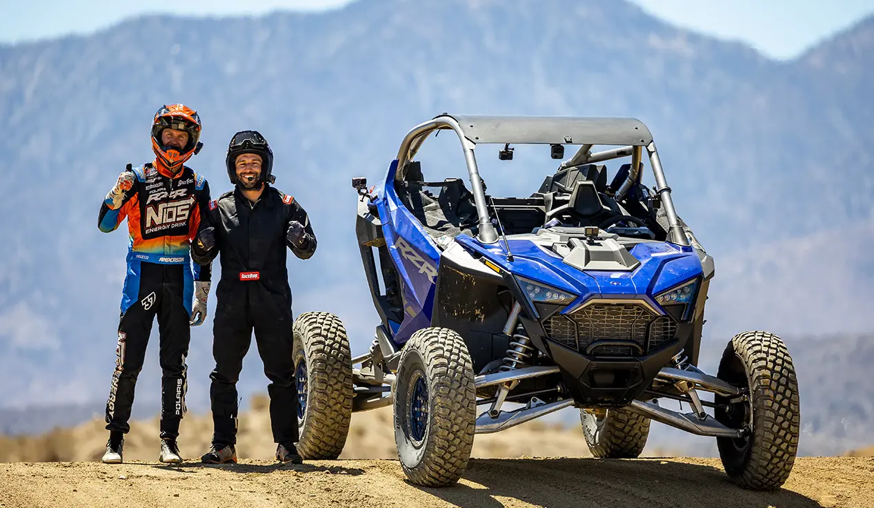 RJ Anderson and other driver smiling and standing next to a RZR