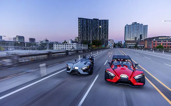 2 polaris slingshot s three wheeled motorcycles driving down a highway