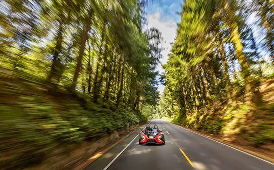 Polaris Slingshot Signature LE conducida en una carretera en un bosque