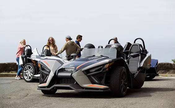group of people hanging out around their polaris slingshot slr three-wheeled motorcycles