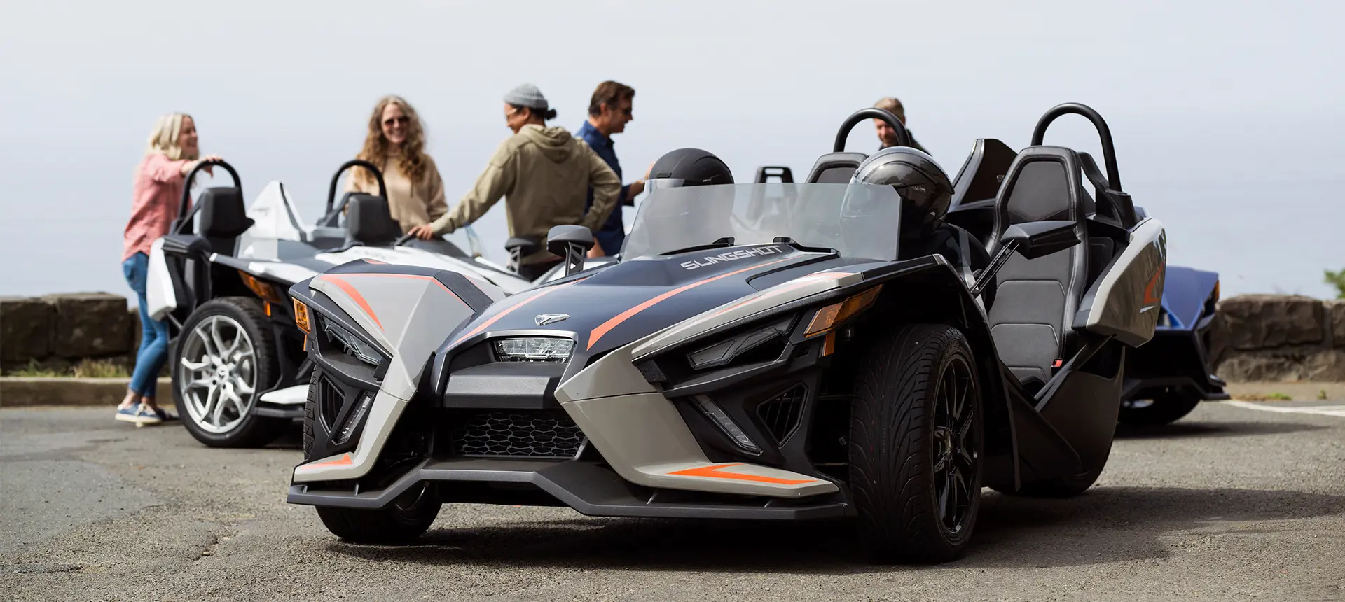 group of people hanging out around their polaris slingshot slr three-wheeled motorcycles