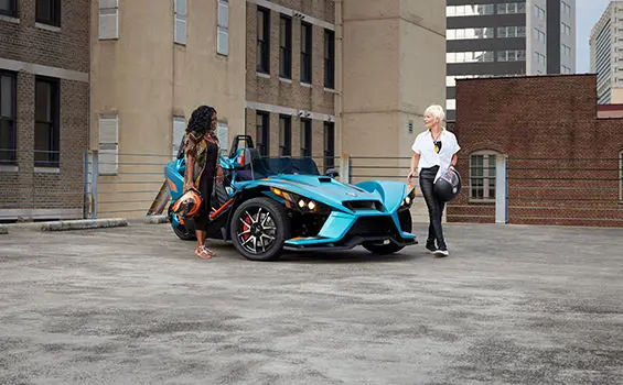 Deux femmes s’éloignant d’une moto à trois roues polaris slingshot r sarcelle pacifique
