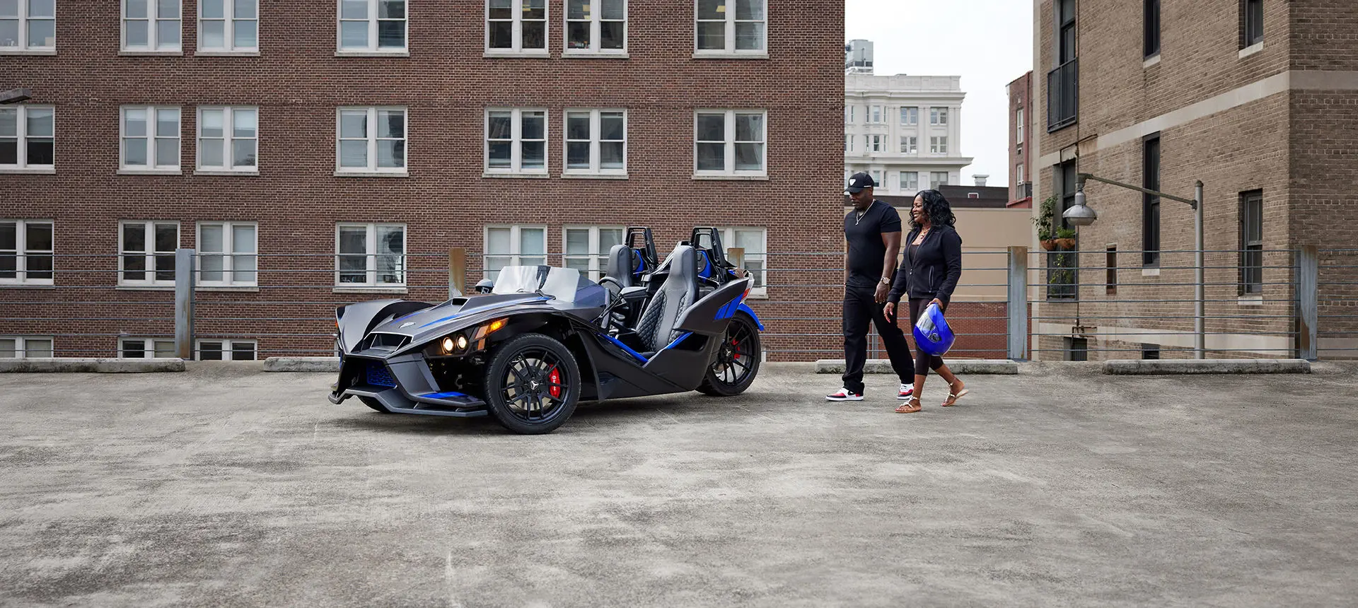 un couple marchant vers un roadster polaris slingshot r à trois roues bleu graphite