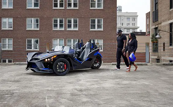 un couple marchant vers un roadster polaris slingshot r à trois roues bleu graphite