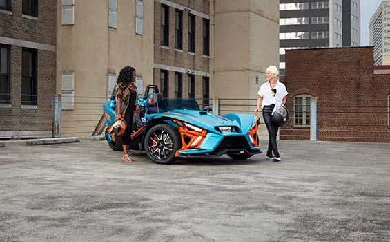 2 women walking away from a pacific teal haze polaris slingshot r three-wheeled motorcycle