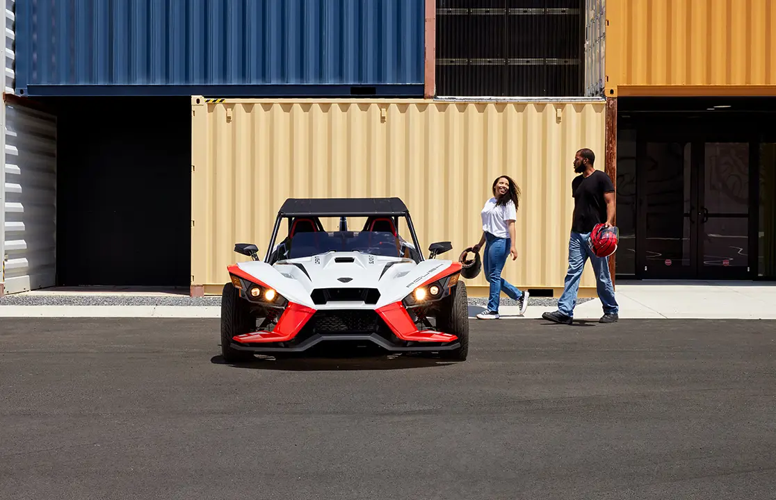 side profile of two 2024 polaris slingshot ROUSH® edition three-wheeled motorcycles cruising down a city street