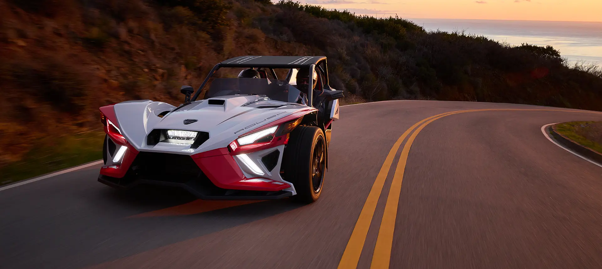 couple driving a Slingshot ROUSH® Edition on a coastal highway