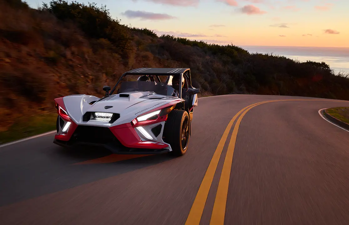 couple driving a Slingshot ROUSH® Edition on a coastal highway