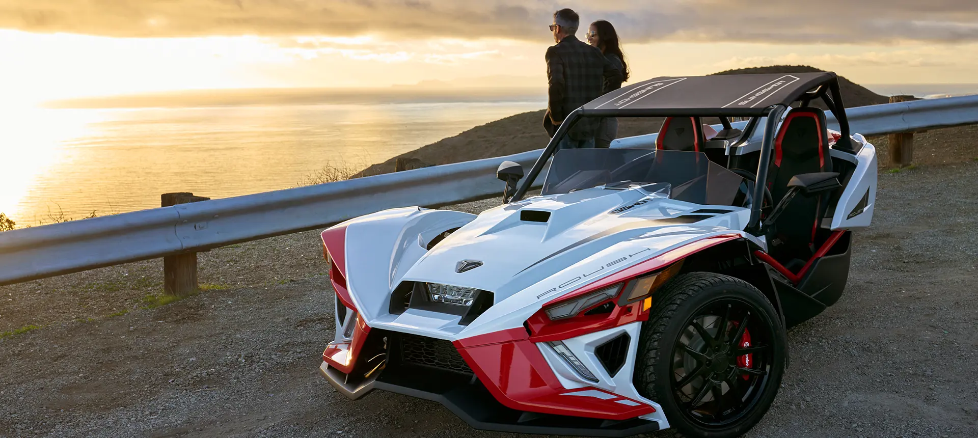 a couple leaning on a Slingshot ROUSH® Edition while looking at a sunset