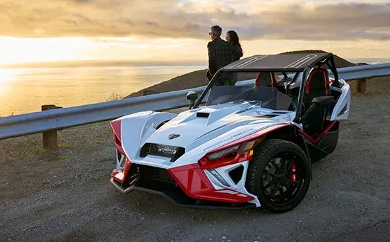 a couple leaning on a Slingshot ROUSH® Edition while looking at a sunset