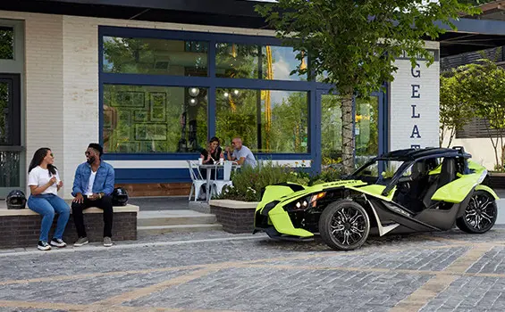 a couple sitting in front of a neon lime polaris slingshot sl three-wheeled motorcycle