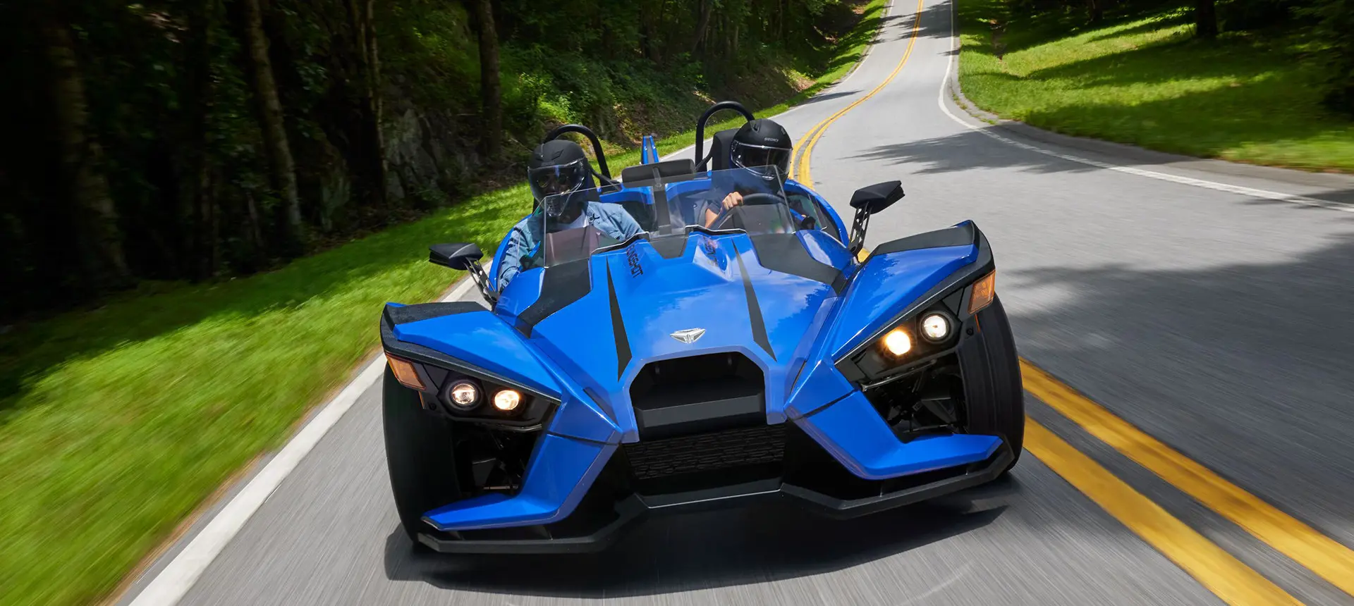 front view of 2 riders in a cobalt blue polaris slingshot sl three-wheeled motorcycle