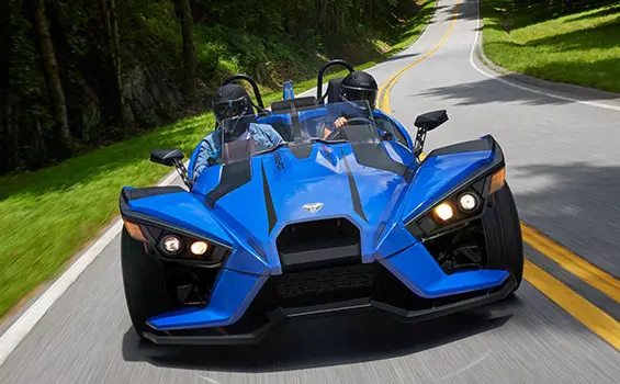 front view of 2 riders in a cobalt blue polaris slingshot sl three-wheeled motorcycle