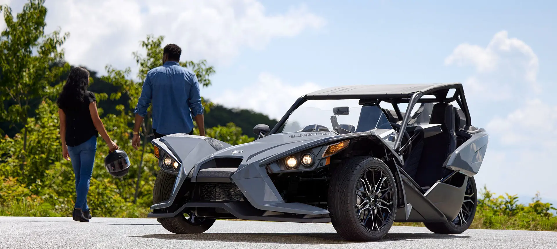 A couple walking away from a storm gray polaris slingshot sl three-wheeled motorcycle