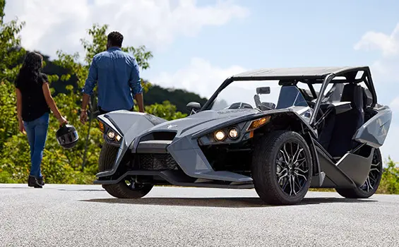 A couple walking away from a storm gray polaris slingshot sl three-wheeled motorcycle