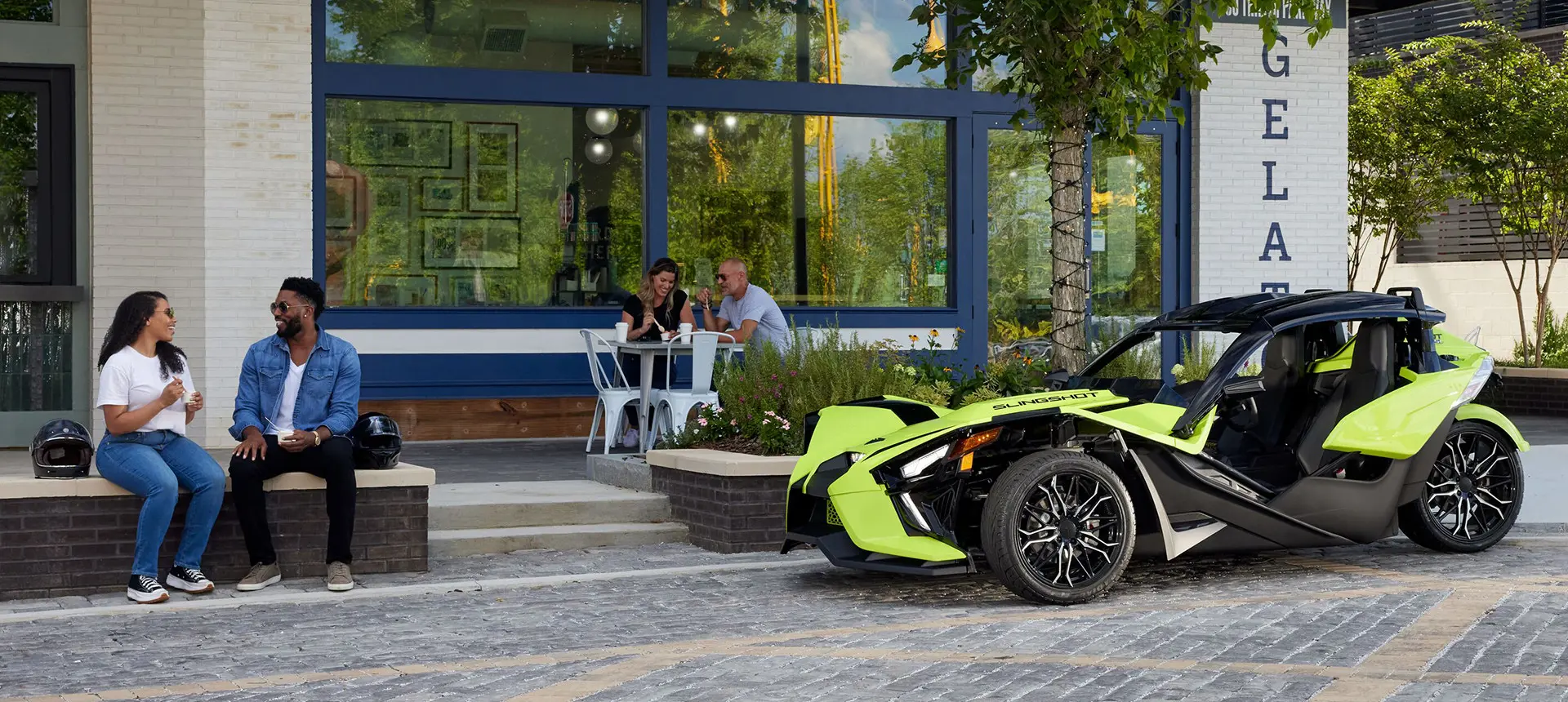 una pareja sentada frente a una motocicleta de tres ruedas de polaris slingshot sl color lima neón