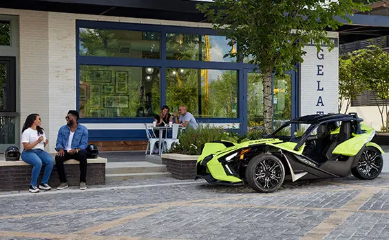 una pareja sentada frente a una motocicleta de tres ruedas de polaris slingshot sl color lima neón