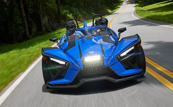 Pareja alejándose de una motocicleta de tres ruedas polaris slingshot en color gris tormenta