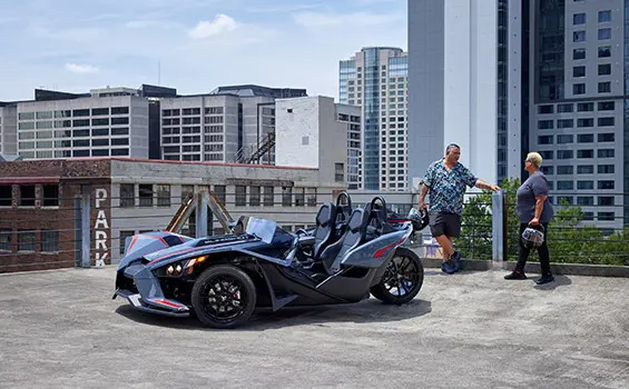 un couple se tenant près d’une moto à trois roues polaris slingshot slr ombrée rouge