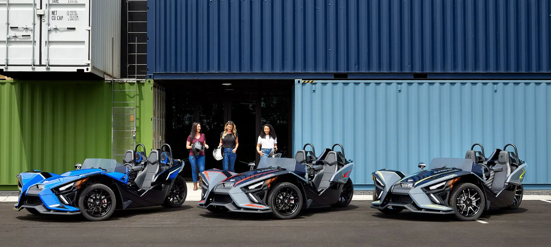 3 mujeres paradas junto a sus roadsters polaris slingshot slr