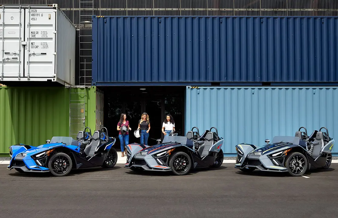 3 mujeres paradas junto a sus roadsters polaris slingshot slr