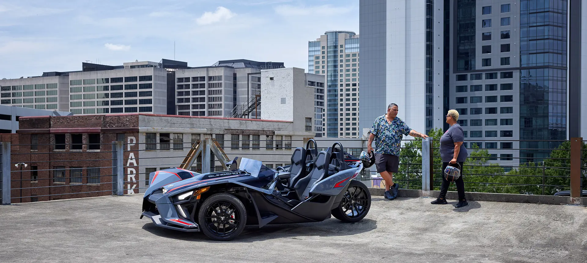 una pareja en una sombra colorada cerca de una motocicleta de tres ruedas polaris slingshot slr