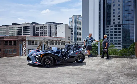 una pareja en una sombra colorada cerca de una motocicleta de tres ruedas polaris slingshot slr