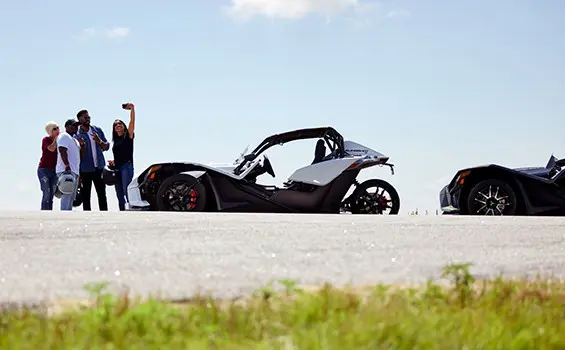 friends taking a selfie in front of hteir polaris slingshot three-wheeled motorcycles