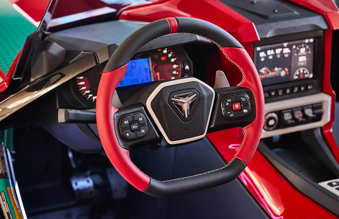 Profil de deux personnes dans un cabriolet Polaris Slingshot 10 2025 circulant sur une grande route.
