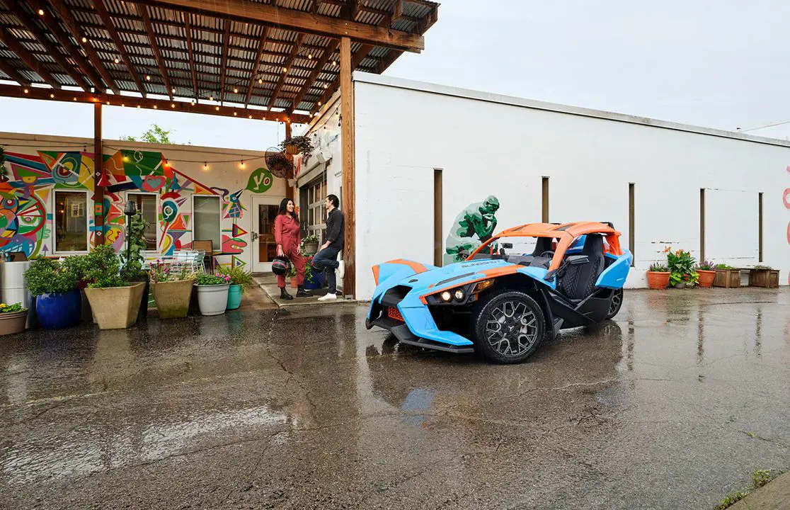 two friends standing near their polaris slingshot sl three-wheeled motorcycle