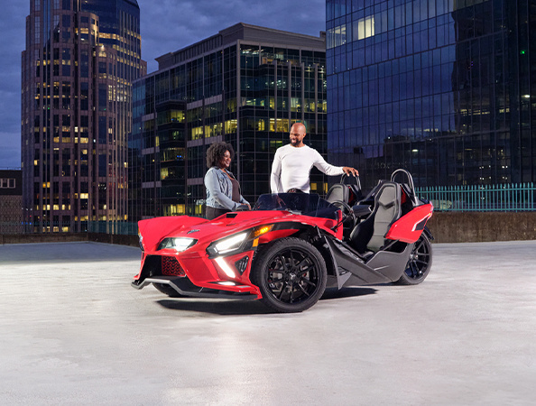 Two people standing around a red and black Slingshot.