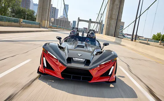 Front-end focused view of a 2025 Polaris Slingshot R three-wheeled roadster cruising down a city street.
