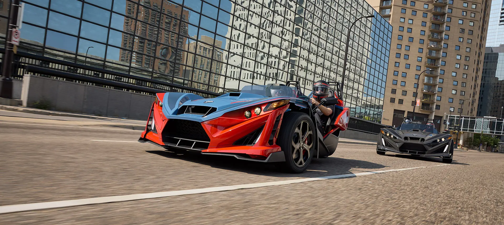 Two 2025 Polaris Slingshot R three-wheeled roadsters cruising down a city street.